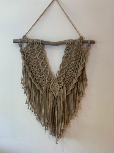 Tapiz de macramé en tonos marrones, decorado con flecos y formas geométricas.